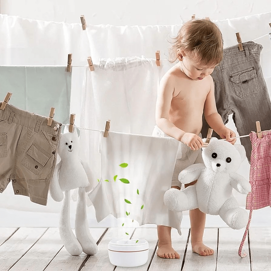 Child playing with a toy bear next to hanging clothes on a wooden floor.