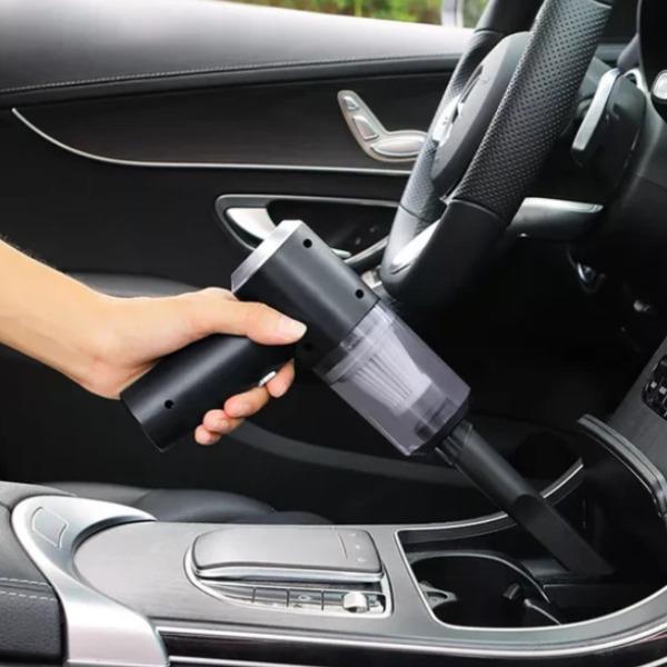 Hand using a black car vacuum cleaner inside a vehicle.