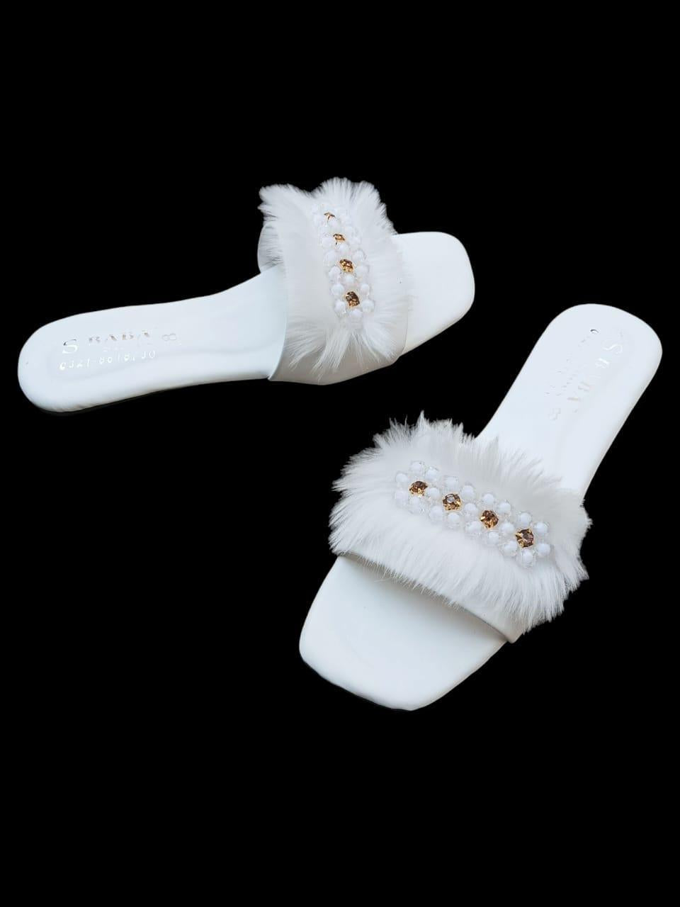White slippers with fluffy fur and gold embellishments on a black background