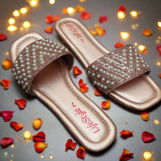 Pair of rose gold sandals with pearl embellishments on a black background