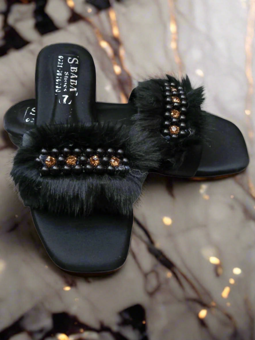 Black slippers with fur and embellishments on a marble surface