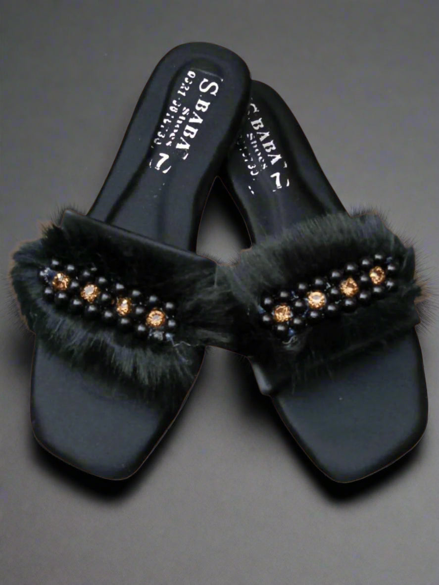 Black sandals with fur and embellishments on a beige background