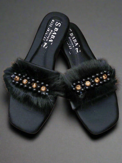 Black sandals with fur and embellishments on a beige background