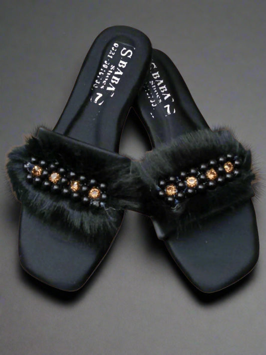 Black sandals with fur and embellishments on a beige background