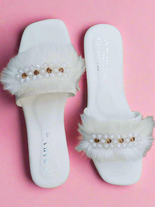 White slippers with fluffy fur trim and decorative beads on a brown background